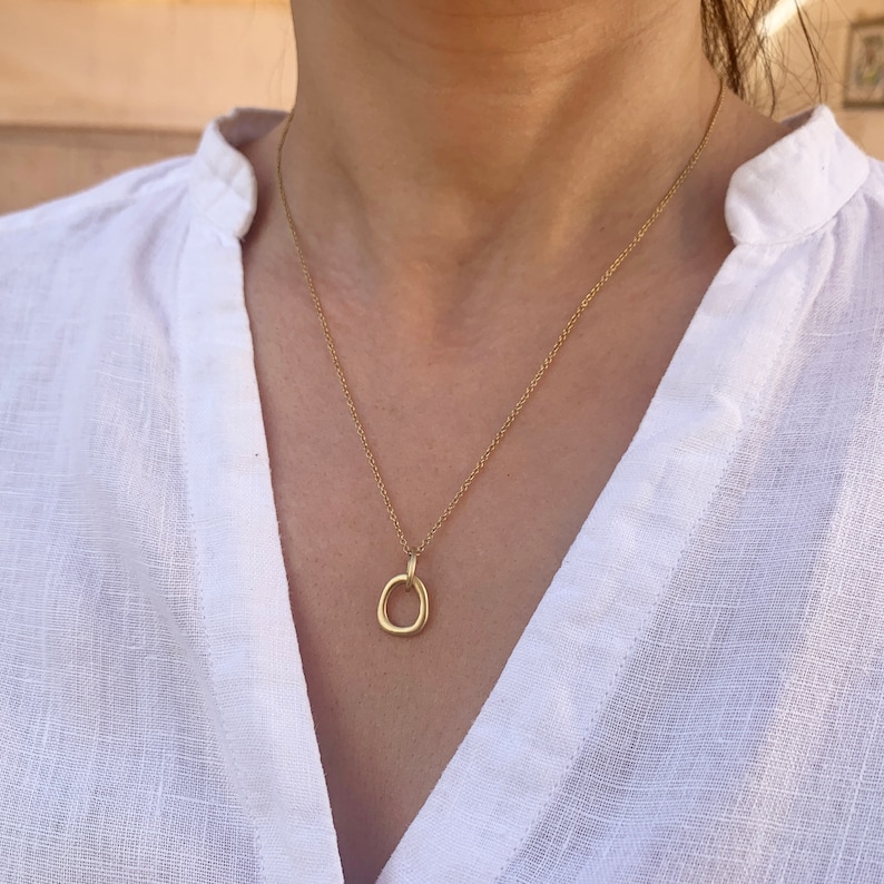 May include: A gold chain necklace with a simple, organic-shaped pendant. The pendant is a circle with a slightly irregular shape.