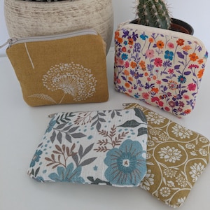 Könnte beinhalten: Vier kleine Reißverschlusstaschen mit floralen und botanischen Mustern. Eine senfgelbe Tasche zeigt ein weißes Pusteblumen-Design. Eine andere hat einen bunten Blumendruck auf cremefarbenem Hintergrund. Die anderen beiden Taschen haben blau-grüne Blumenmuster.