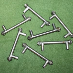 May include: Eight silver cabinet pulls with a decorative beaded design. The pulls are in a variety of positions, showing the different angles of the design.