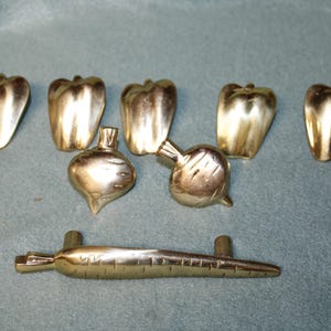 May include: A collection of eight brass cabinet knobs and pulls shaped like vegetables. The set includes five bell pepper knobs, two round radish or turnip knobs, and one long carrot-shaped drawer pull, all featuring a polished metallic finish.