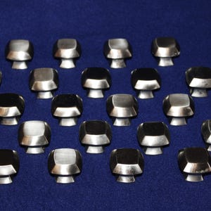 May include: A collection of twenty-one silver and black cabinet knobs with a geometric design. Each knob has a square top and a cylindrical base. The knobs are arranged on a dark blue background.