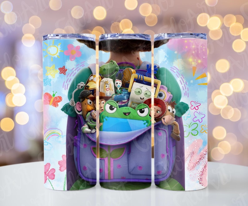 May include: A cylindrical tumbler featuring a colourful graphic print of a purple backpack filled with various cartoon characters, including a green frog, a cowboy, a space ranger, and a potato figure, surrounded by drawings of flowers and a rainbow.