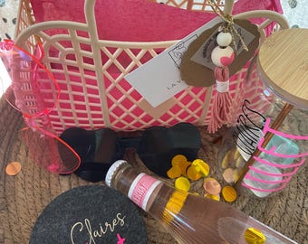 May include: A gift basket with a pink plastic tote, sunglasses, a bottle of Lillet Rosé, a glass with a wooden lid, and a coaster with the name "Claires Lillet". The basket contains pink tissue paper and gold confetti.