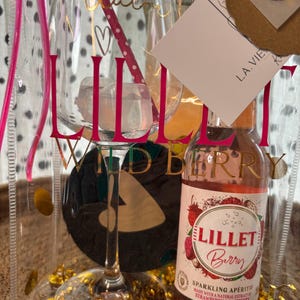 K&ouml;nnte beinhalten: Ein transparentes Geschenkset mit einem Weinglas, einer Flasche Lillet Berry Sektaperitif und einer transparenten Tragetasche. Das Weinglas tr&auml;gt das Wort "Lillet" in Rosa. Die Tragetasche tr&auml;gt die Worte "La Vie" und "Claire's Kreations".