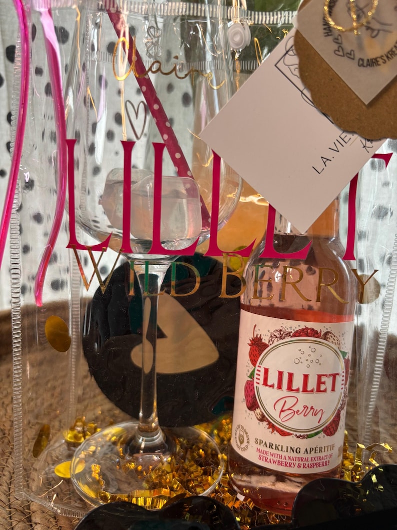 K&ouml;nnte beinhalten: Ein transparentes Geschenkset mit einem Weinglas, einer Flasche Lillet Berry Sektaperitif und einer transparenten Tragetasche. Das Weinglas tr&auml;gt das Wort "Lillet" in Rosa. Die Tragetasche tr&auml;gt die Worte "La Vie" und "Claire's Kreations".