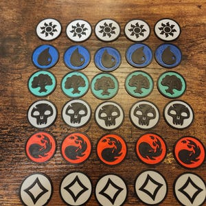 Peut inclure: Une collection de jetons imprimés en 3D avec divers symboles, notamment des soleils, des gouttes d'eau, des arbres, des crânes et des flammes tourbillonnantes. Les jetons sont en blanc, noir, bleu, rouge et sarcelle, et sont disposés sur une surface en bois. Ces jetons sont probablement pour un jeu de société.