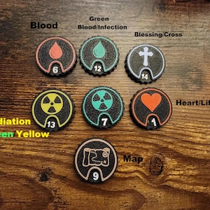 Pu&ograve; includere: Sette gettoni da gioco circolari neri con bordi testurizzati. Ogni gettone presenta un'icona unica: una goccia di sangue rossa, una goccia di sangue verde, una croce bianca, un simbolo di radiazione giallo, un simbolo di radiazione verde, un cuore arancione e una mappa bianca.
