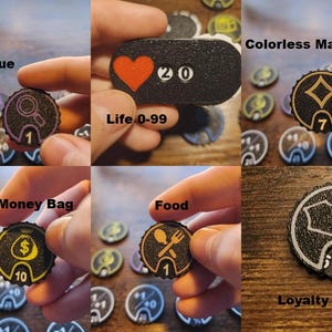 Pu&ograve; includere: Una collezione di gettoni da gioco neri circolari e rettangolari con varie icone e numeri. I gettoni mostrano simboli per Clue, Life 0-99, Colorless Mana, Tax/Money Bag, Food e Loyalty, con grafiche bianche e colorate su superfici testurizzate.