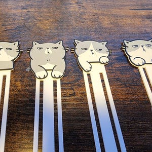May include: Four gray cat-shaped bookmarks with white stripes. Each bookmark has a different expression on its face.
