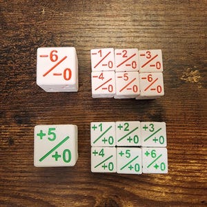 May include: A collection of white six-sided dice featuring red and green numerical markings. The red dice display negative numbers with a slash and zero, while the green dice show positive numbers with a slash and zero, arranged in rows.