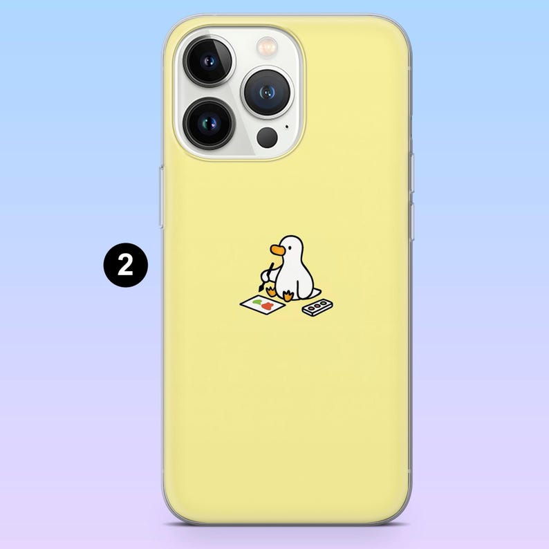 May include: Yellow phone case featuring a cartoon duck artist illustration. The duck is painting on a small canvas with a palette and a remote control. The phone case has a clear border and a number 2 in a black circle.
