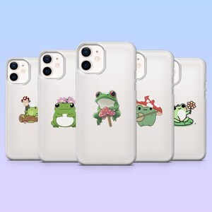 May include: A collection of five clear phone cases, each featuring a different cartoon frog design. The frogs are depicted with various accessories, including a mushroom, flowers, and a lily pad. The cases are designed to fit a smartphone.