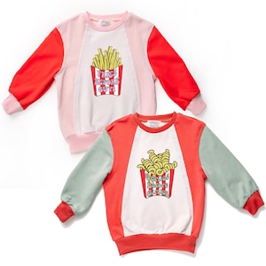 Może przedstawiać: Dwie bluzy w stylu color block. Jedna jest różowo-czerwona z grafiką frytek i napisem "Fries Before Guys". Druga jest czerwono-zielona z grafiką frytek czosnkowych i napisem "Garlic Before Girlies".