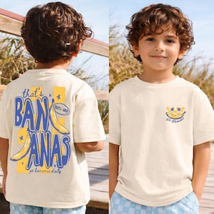May include: A cream-coloured t-shirt with a banana graphic and the text "that's BANANAS" in blue and yellow. The shirt also features a small banana graphic with the text "go bananas daily". The front of the shirt has a banana graphic with stars.