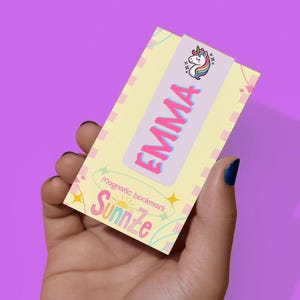 May include: A magnetic bookmark with the name "EMMA" in pink and blue lettering. The bookmark features a unicorn illustration and the text "Sunnze". The background is light yellow with pink and green accents.
