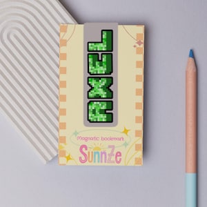 May include: A magnetic bookmark featuring the word "EXCEL" in green pixelated letters. The bookmark is set against a light yellow backdrop with a decorative border and the pink script word "Sunnze". A blue pencil is in the background.