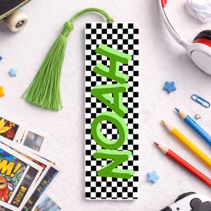 May include: A personalised bookmark featuring the name "NOAH" in green 3D lettering. The bookmark has a black and white chequered pattern and a green tassel. A reading accessory.