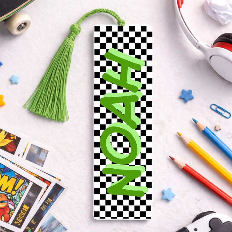 May include: A personalised bookmark featuring the name "NOAH" in green 3D lettering. The bookmark has a black and white chequered pattern and a green tassel. A reading accessory.