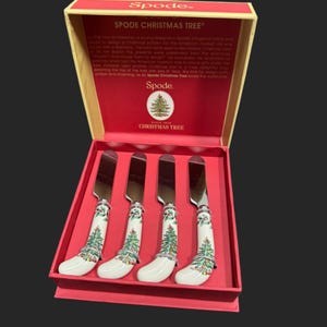 May include: A set of four Spode Christmas Tree butter knives in a red and gold box. The knives have white handles decorated with a Christmas tree design and silver blades. The box features the Spode logo and Christmas Tree branding.