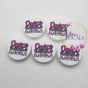 May include: Five white circular buttons with the words "Dance MOM" in pink and black leopard print. The text is in a stylized font. The buttons are arranged on a white background.