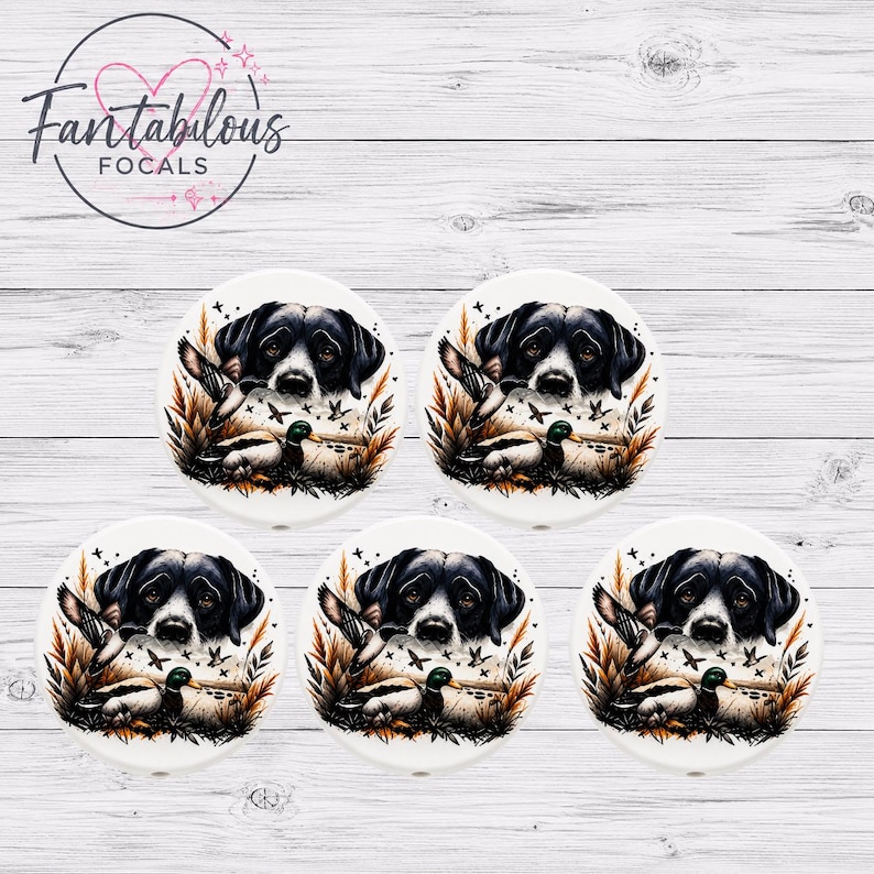 May include: Five white ceramic coasters with a hunting dog design. The design features a black and white dog, ducks, and foliage in shades of brown and green. The coasters are arranged on a white wood-grain surface. The top left corner has the text "Fantabulous Focals".