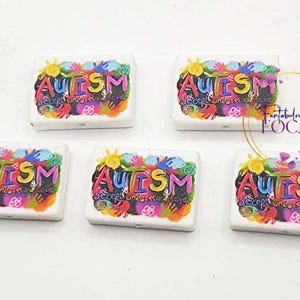 May include: Five white rectangular objects with the word "AUTISM" in colorful letters. The word "Accept Understand Love" is also visible. The objects have a vibrant, artistic design with a variety of colors.