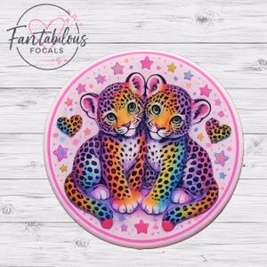 May include: A circular button featuring two rainbow-colored leopard cubs sitting side by side. The design includes colorful stars and two leopard-print hearts on a light pink background. The text Fantabulous FOCALS is printed in black.