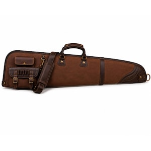 Può includere: Una custodia lunga per arma da fuoco di colore marrone con maniglia superiore, tracolla rimovibile e due tasche frontali con fibbie e finiture color ottone. L'esterno è realizzato in materiale testurizzato con cuciture rinforzate e un anello a D.