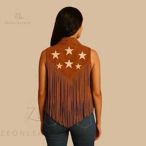 May include: Brown suede vest with white star design and fringe. The sleeveless vest features a collared neckline and a decorative star pattern on the back. The bottom of the vest has long fringe.
