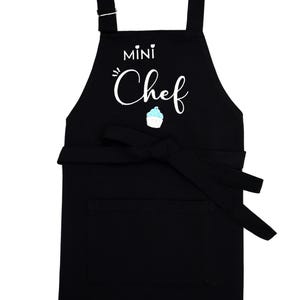 Pu&ograve; includere: Grembiule nero con la scritta bianca "MINI Chef" e un'illustrazione di cupcake. Ha una tasca frontale e un cinturino regolabile per il collo, perfetto per i giovani cuochi.