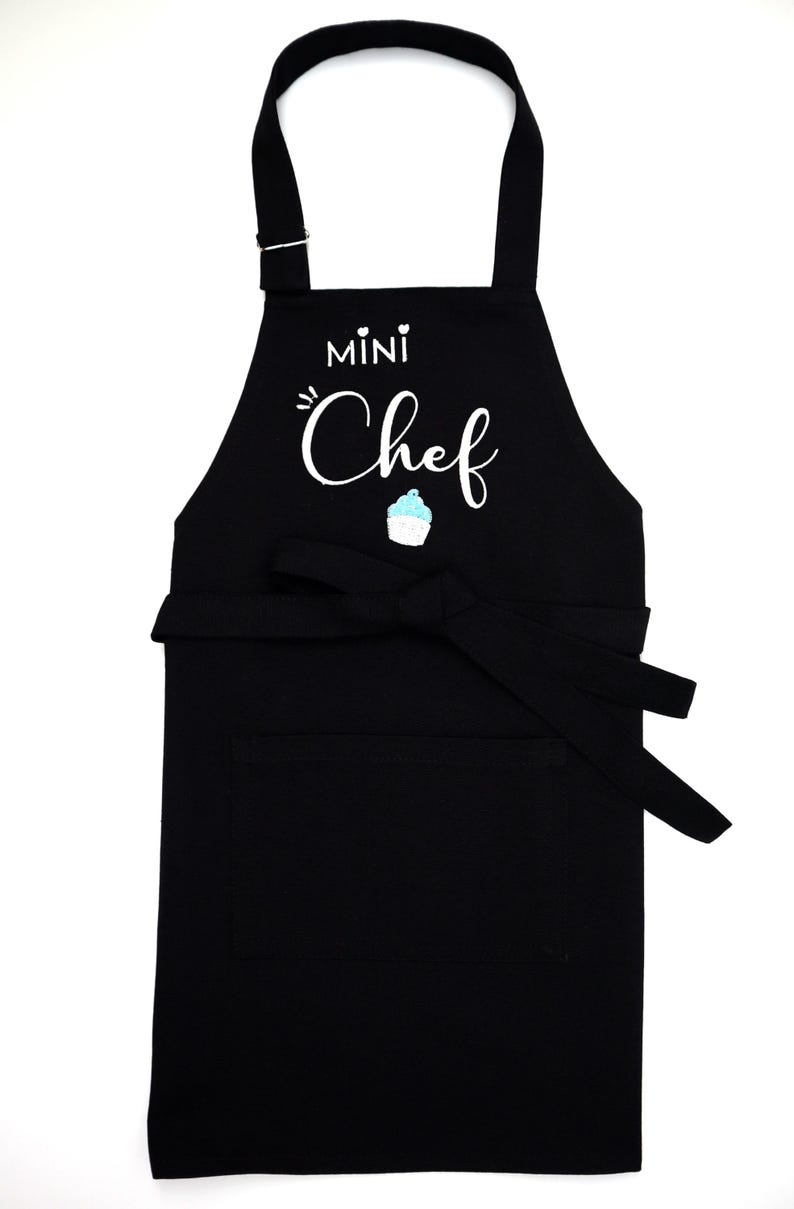 Pu&ograve; includere: Grembiule nero con la scritta bianca "MINI Chef" e un'illustrazione di cupcake. Ha una tasca frontale e un cinturino regolabile per il collo, perfetto per i giovani cuochi.