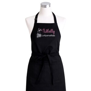 May include: Black apron with a neck strap and waist ties. The apron features a pink and white logo that reads "Xitlally LollysnailLab". The apron has two front pockets and is displayed on a mannequin.