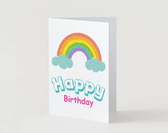May include: White greeting card with a colorful rainbow and blue clouds. The card reads "Happy Birthday" in turquoise and pink lettering. The card is folded and stands upright.