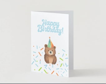 May include: A folded birthday card with a light blue "Happy Birthday!" text. A brown bear wearing a party hat is centered below the text. Colorful confetti-like shapes are scattered around the bear.