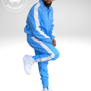 Puede incluir: Un ch&aacute;ndal azul claro con rayas blancas en los laterales. La chaqueta tiene cuello y los pantalones tienen cintura con cord&oacute;n. El conjunto se combina con un gorro de pescador a juego y zapatillas altas blancas. El conjunto es de estilo deportivo e informal.