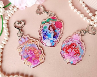 May include: Three colorful keychains featuring Disney princesses. Each keychain has a different princess: Belle, Ariel, and Rapunzel. The keychains are made of clear acrylic and have a silver metal chain.