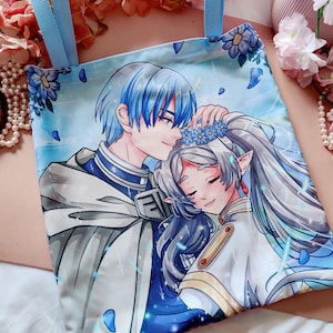 May include: Light blue tote bag with a romantic anime-style illustration of a couple. The artwork shows a man with blue hair and a woman with long silver hair, embracing. The bag has light blue handles and floral accents.