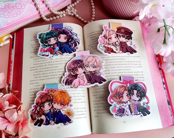 May include: An open book with several anime-style couple bookmarks. The bookmarks feature colorful illustrations of couples in various outfits. The book is surrounded by pink flowers and a pink purse.