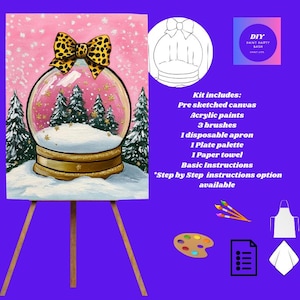 May include: A snow globe painting kit on an easel. The canvas shows a snow globe with a winter scene and a leopard print bow. The kit includes acrylic paints, brushes, an apron, and a palette. The kit also includes a pre-sketched canvas.