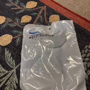 May include: A white plastic bag with a blue Philips Respironics logo. The bag is sealed and has a small hole in the top.