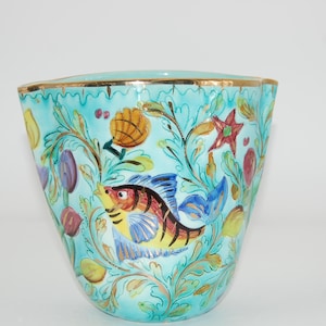Könnte beinhalten: Eine türkisfarbene Keramikvase mit Goldrand, verziert mit einem handgemalten Design eines Fisches, Muscheln und botanischen Elementen. Die Vase hat eine einzigartige Form und eignet sich für dekorative Zwecke.