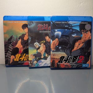 Puede incluir: Tres estuches de discos Blu-ray con ilustraciones de anime. Los estuches son azules y presentan texto japonés e ilustraciones de personajes musculosos. Los títulos incluyen "Fist of the North Star" y "Fist of the North Star 2".