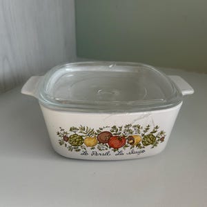May include: White rectangular casserole dish with a clear glass lid. The dish features a colorful vegetable and herb design with the text "Le Persil, La Sauge". The dish has two handles.
