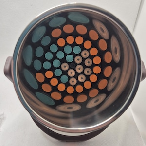 May include: Stainless steel insulated container with a brown handle. The interior features a pattern of teal and orange circles, with a central arrangement of smaller, light-colored circles. The container is designed to keep contents at a consistent temperature.