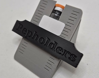 May include: A gray 3D-printed holder with a black label that reads "Pepholders". The holder is designed to hold a small glass vial with an orange cap. The holder has a rectangular shape with angled sides and a slot for the vial.
