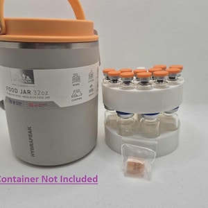 May include: A gray 32oz stainless steel insulated food jar with an orange handle and lid. Next to it is a white rack holding multiple small glass vials with orange caps. A small plastic bag contains a few small orange tablets.