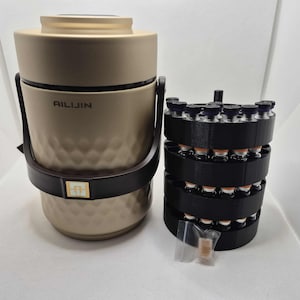 May include: A beige insulated container with a black handle and the text "AILIJIN". Next to it is a black multi-tiered holder filled with small glass vials. A small clear bag with a brown object is in front.