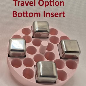 May include: A pink, circular travel option bottom insert with multiple round holes and four stainless steel cubes. A small, light pink cylinder is in the center. The text "Travel Option Bottom Insert" is in red.