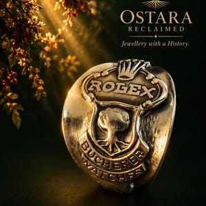 Puede incluir: Un anillo de metal plateado con un emblema en relieve que presenta el texto ROLEX en la parte superior, un motivo de árbol central y el texto BUCHERER WATCHES en la parte inferior. El fondo muestra el texto OSTARA RECLAIMED Jewellery with a History.