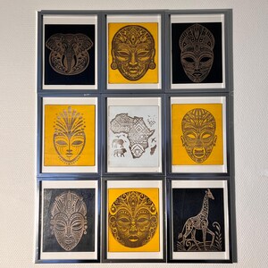May include: Nine framed black and gold prints with African-inspired designs. The prints feature masks, animals, and a map of Africa. The frames are silver and have a black mat.